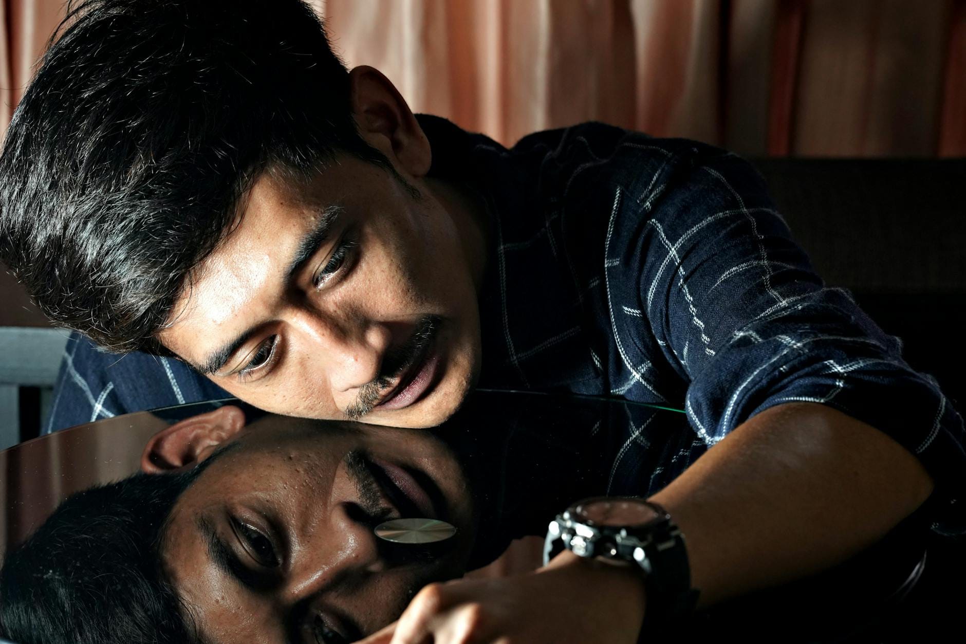 Zamyślony mężczyzna opierający głowę o szklany stół z odbiciem