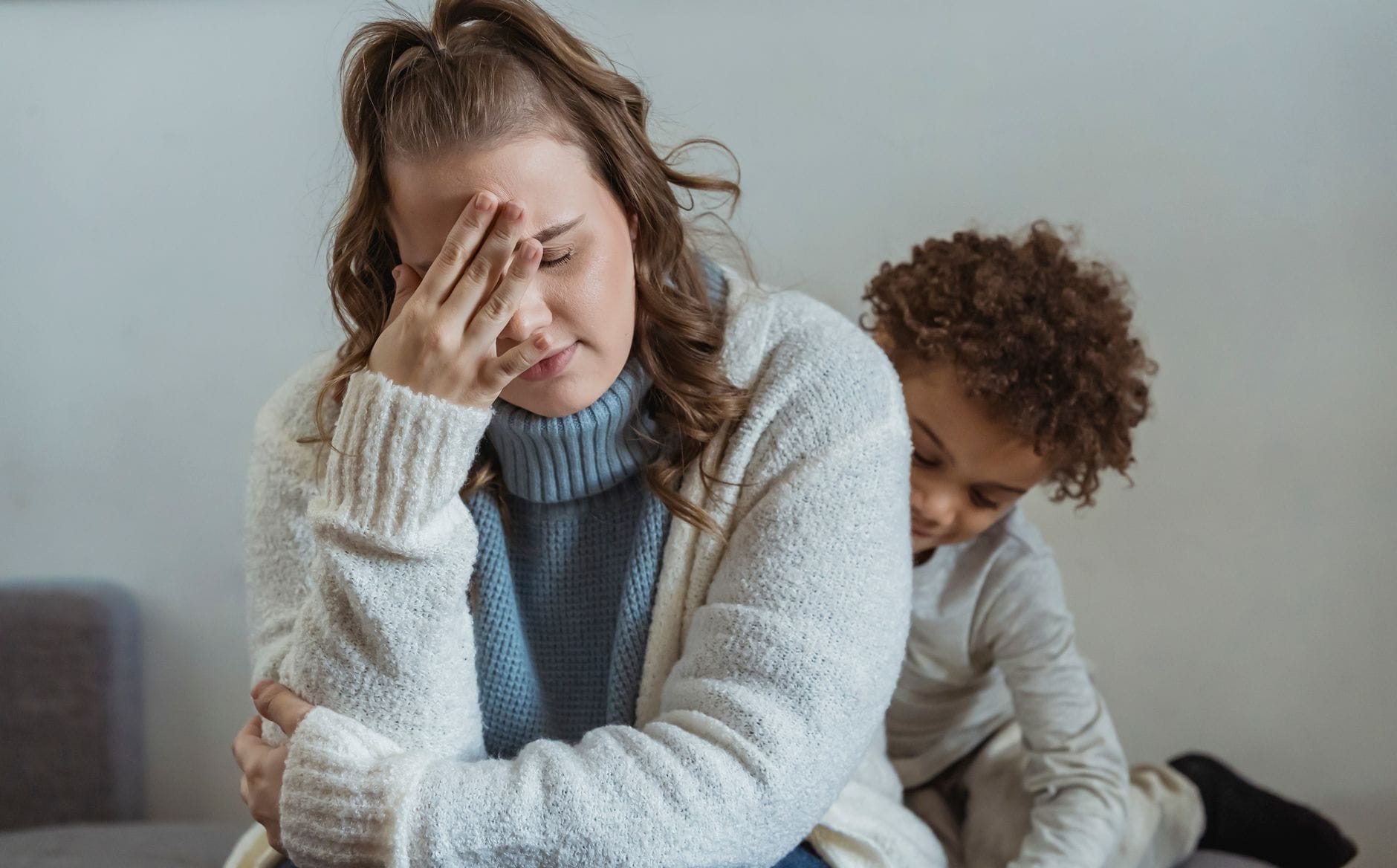 Zmęczona mama z ręką na czole obok syna przy ścianie w domu