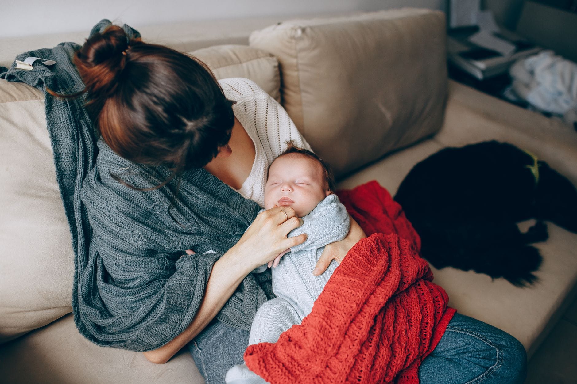 Zmęczona mama przytula śpiące niemowlę na kanapie w salonie