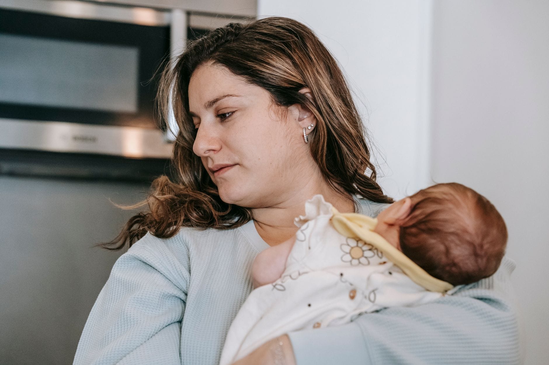 Kryzys po narodzinach dziecka Baby blues depresja poporodowa czy zmęczenie Zmęczona mama z niemowlęciem na rękach stojąca w jasnej kuchni