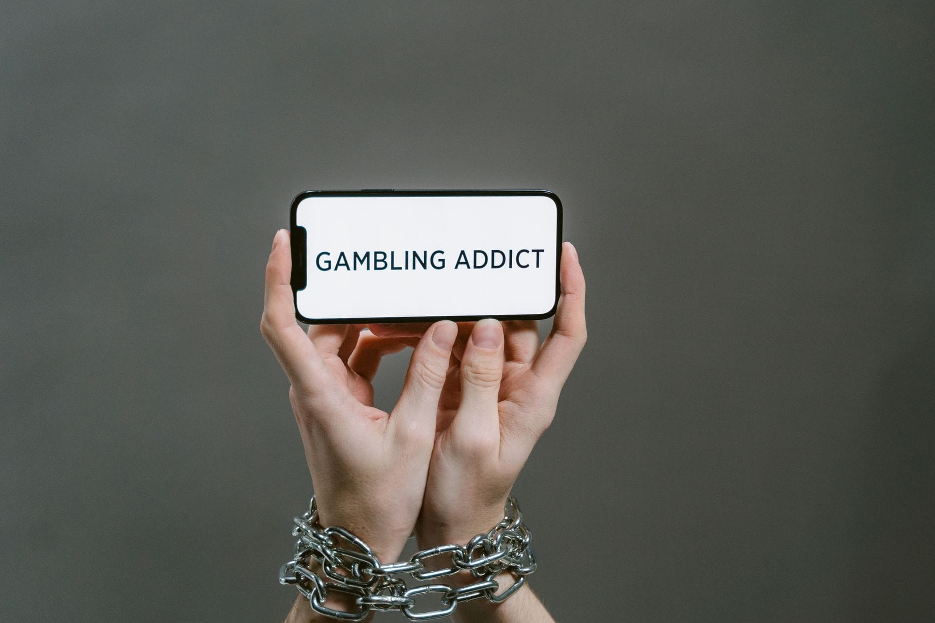 Skrępowane łańcuchem dłonie trzymają telefon z napisem Gambling Addict